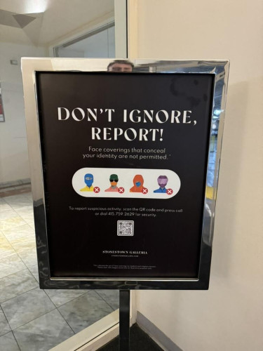 Sign in a shopping mall that reads in all-caps, “Don’t Ignore, Report! Face coverings that conceal your identity are not permitted.”