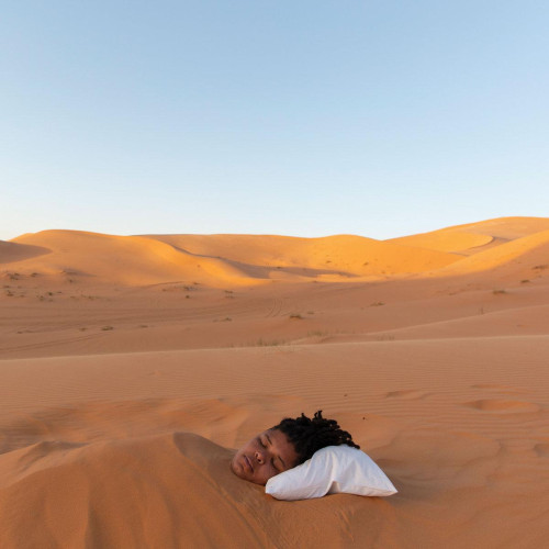 A girl buried in sand in the desert, peacefully sleeping with her head on a pillow