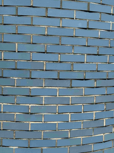 A photo of a brick wall that has been painted ocean blue. The paint is beginning to chip off in some places and never seems to have covered the spaces between the bricks well. This leaves an off-white outline around almost every brick except for the ones that have a little moss growing or grime existing between bricks instead. 
