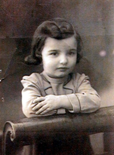 Vintage black and white photo of a young child with curly hair, leaning arms on a horizontal bar and looking directly at the camera. 