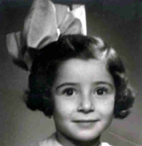 Picture of a young girl's face. Her eyes are wide open. Her dark hair reaches behind her ears and she has a large bow on her head.