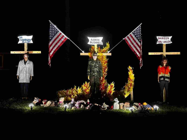 Three people on crosses. In the center is an effigy of Aaron Bushnell with two American flags wreathed in flames. On either side are Dr Hamman Alloh and Shireen Abu Akleh.