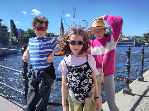 3 kids facing the camera, with water in the background, in Stockholm.