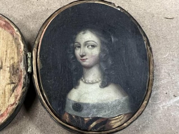 Tiny painting inside an open pendant. Portrait of a young woman, obviously very wealthy, in a fancy dress, with dark hair worn down, in ringlets. She's looking sharply off to the side, and smirking. The whole vibe is very "Mona Lisa, if Mona Lisa was the life of the party". 