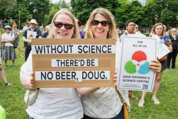 Two people holding up as hand written 2 signs that read "Without Science there'd be not beer, Doug. 
The other is a protest sign to "Save the Ontario Science Centre"