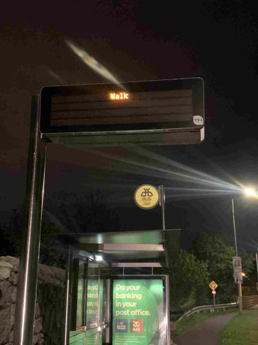 Digital sign over a darkened bus stop that says only WALK 