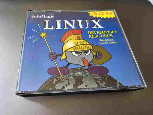 This is a photo of a 6-CD set case for "InfoMagic LINUX Developer's Resource". The CD case cover has a whimsical cartoon character on the front, which appears to be an anthropomorphic penguin dressed as a wizard, complete with a wizard's hat and a magic wand. The character is standing on a stylized representation of the globe. The background is blue and there is a yellow banner on the top right corner that says "QuickStart Guide inside". The packaging suggests that this is a software resource kit for Linux developers from the era when software was commonly distributed on CDs.