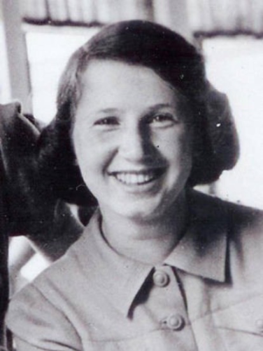 A portrait photo of a woman. You can see her face and shoulders. She has a wide smile and is looking directly into the camera. She has hair reaching behind her years. The shirt is buttoned up with two large buttons.
