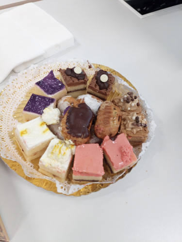 Photo of a plate of little squares of cake filling the circle in various colours and varieties. There's also small pastries like profiteroles as well.