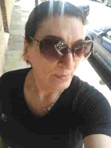A selfie of a woman running in the sun  in a Karimoor black top and brown sunglasses