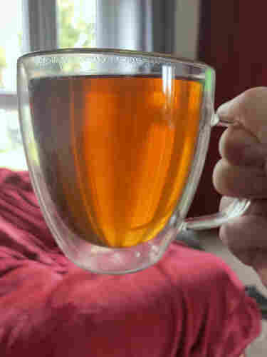A close-up of a person holding a clear glass mug filled with amber-colored Jin Jun Mei tea.