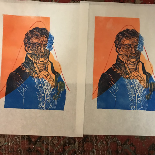 As described, a photo of two linocut prints drying on my floor with worn red patterned carpet. The prints are on white washi paper 30 cm by 40 cm and have one large section of a circle and several varied smaller overlapping circles in tints and shades of pale orange to pale golden yellow-orange. Fourier is printed in blue ink on top of these orange circles and dressed in 18th century garb. A red sinusoidal function is printed on top such that his head finds within a crest and the throughs to either side frame him.
