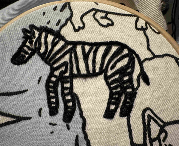 A small embroidered zebra. The stripes are done in black thread, but the white fabric background is unworked. 