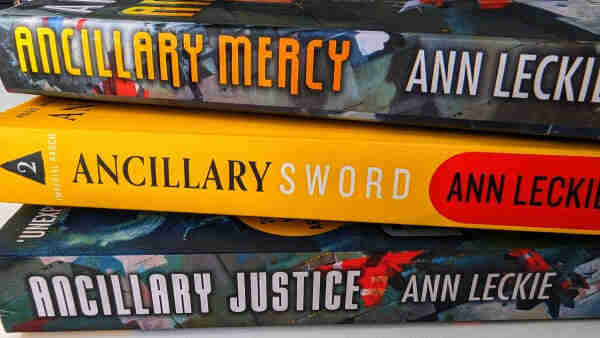 Three books by Ann Leckie sitting on top of each other. Ancillary Justice on the bottom, Ancillary Sword in the middle and Ancillary Mercy on top.