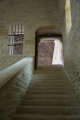 A stone staircase, leading up to a large hall with a barrel-vaulted roof. There is a barred window to the left of the staircase.