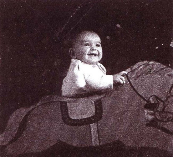A vintage photograph capturing a joyful baby sitting on a rocking horse, exuding a sense of delight and innocence.