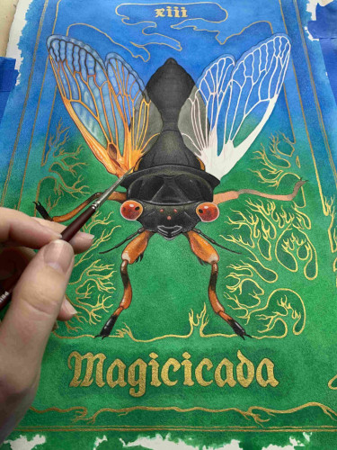 A painting in progress of a tarot card style poster of a periodical cicada. The genus name, Magicicada, is underneath it, and the number 13 is at the top in Roman numerals. A hand holding a paintbrush is in the foreground. 