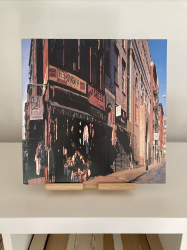 A vinyl record cover with a photograph of a street scene with various storefronts, including, on the corner, a clothes shop called "Paul's Boutique." The shops are situated in a brick building, and there are clothes and items displayed on the sidewalk.