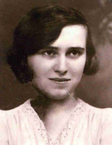 Portrait photograph of a young woman. She is wearing a white blouse. She has dark hair reaching past her ears. It is slightly wavy. The woman is smiling gently.