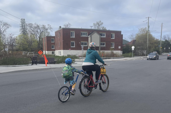 A woman and child cycle to school on a wide street with no cycling infrastructure in the community of Vanier, in Ottawa.