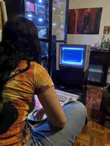 A woman with long, dark hair sitting on a couch, usborne game programming book and C64C in front of her, attachd to a Sony Trinitron PVM.