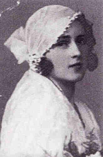 Black and white portrait photograph of a woman in a wedding dress. Her head and shoulders are visible. She has dark hair covered by a white shawl. 