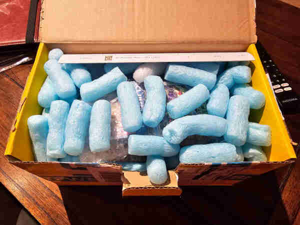 Cardboard box open to show blue packing peanuts. 
