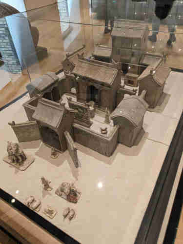 A model of an ancient Chinese home, taken from a tomb. It is made of earthenware and displayed in a glass museum case