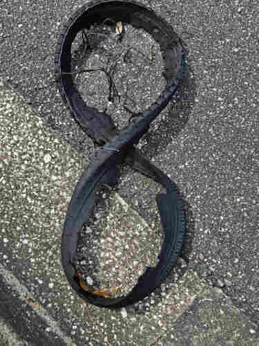 Sidewalk next to a grey gravel asphalt mix roadway over the thin rubber and wire remains of a tire, twisted into a figure 8. 

eight ... ha ha ha - read in the voice of The Count from Sesame Street.