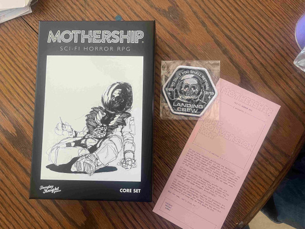 A tabletop role-playing game 'Mothership Sci-Fi Horror RPG' core set box with artwork of an astronaut, a 'Landing Crew' patch on the right, and a pink character sheet for the game.