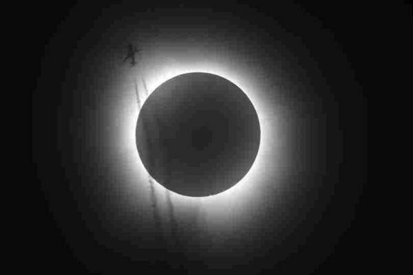 A plane leaving contrails below a solar eclipse.  Note the slight distortion of the contrails inside the shadow.