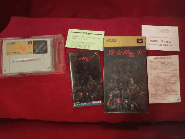 Full boxset of Shin Megami Tensei (1) (Sufami) - cartridge in left, manual book in center, some instruction paper above, the boxset on the right of it, and two information and instruction paper on the right.
