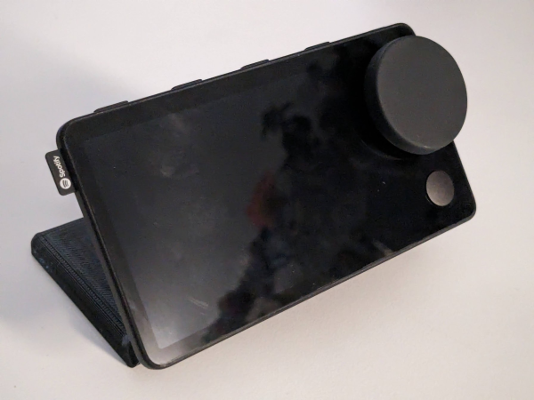 Photo of the Spotify CarThing attached to a black 3D printed desktop stand, showing the front view.