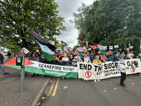 Large crowd with flags and placards march behind banners reading CEASEFIRE NOW and END THE SIEGE IN GAZA