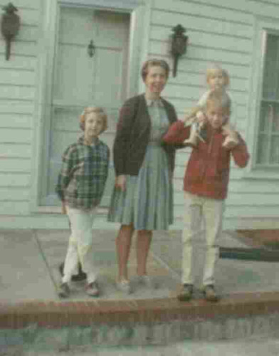 A vintage photo of a woman and three children standing on the front steps of a house.