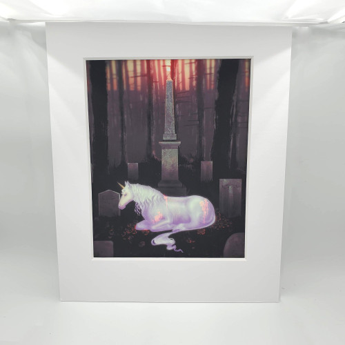 An iridescent unicorn lying in front of a tall pillar style grave during a red-orange sunset. It is in a white mat.