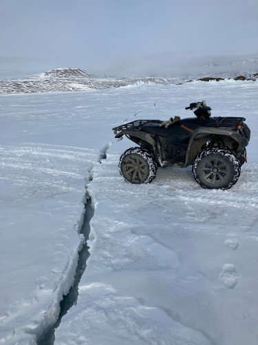 An ATV sits on the frozen Arctic Ocean. From the foreground, running behind the ATV and beyond to a point is a crack in the ice. 