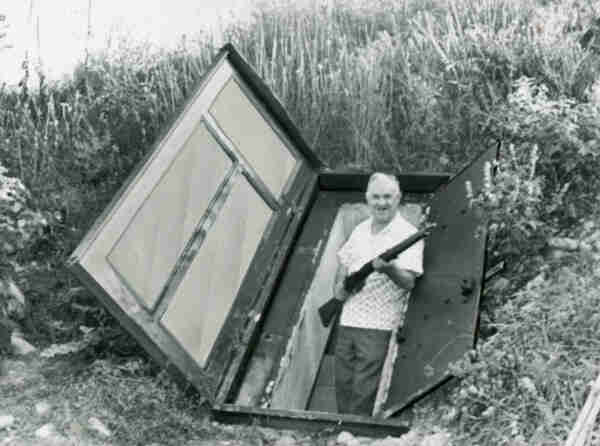 Image of a man coming out of his underground fallout shelter holding a rifle in 1961