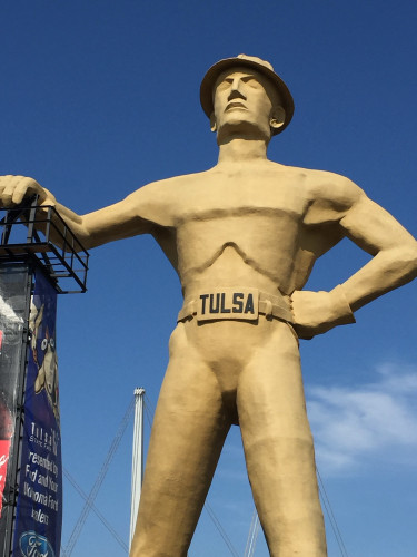 The Golden Driller, in Tulsa, Oklahoma, statue of a person wearing a hard hat and a belt with "TULSA" written on it, set against a clear blue sky.