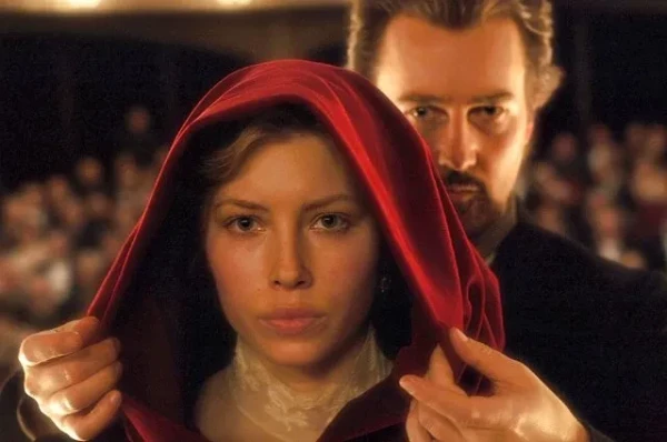 In a scene from The Illusionist, the magician adjusts the hood of a cape over the head of a young woman while on stage.