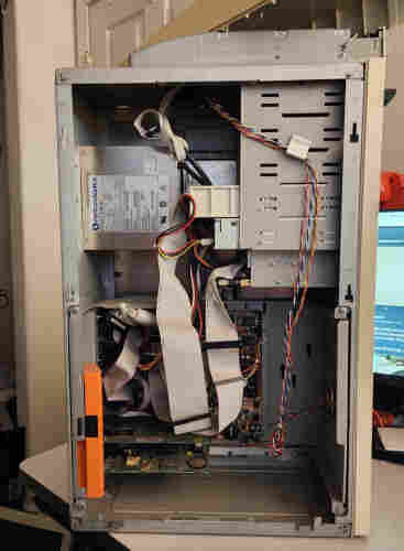 An AT tower, the side panel open. There's a power supply near the top, several drives (HD caddy, CD ROM, 3.5" floppy disk, 3.5" hard drive), then a motherboard at the bottom with lots of ribbon cables