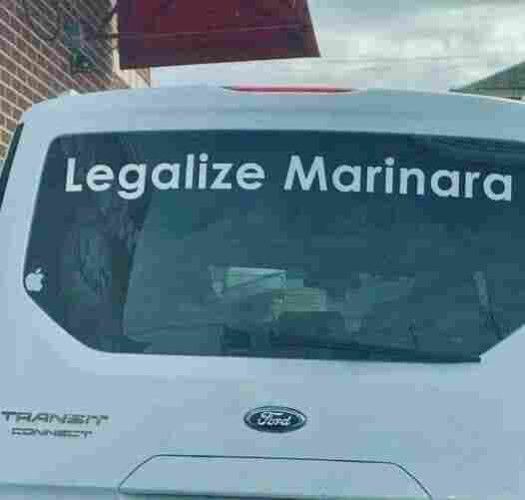 White lettering on the back window of a white Ford Transit van reads: “Legalize Marinara”. 
