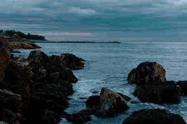 Rocky coastline with calm sea under an overcast twilight sky. This photo is somewhat dim but I think it represents what it was like to stand there in the moment. 