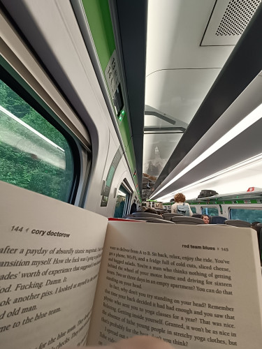 The interior of a british train behind an open physical copy of Red Team Blues