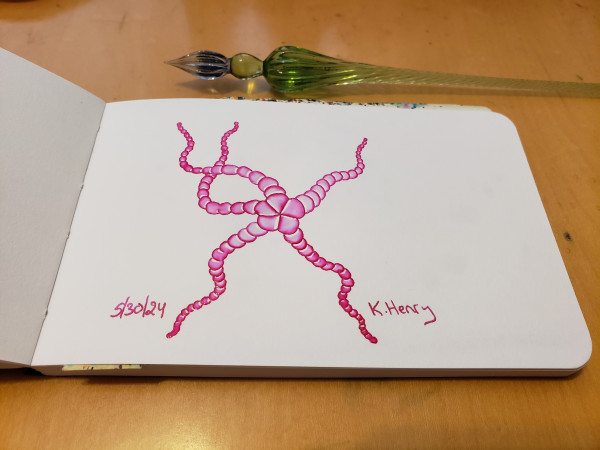 Hand drawn generative/iterative art in ink on an open page of my sketchbook. The abstract pattern looks like a happy dancing starfish. My glass dipping pen is next to my sketchbook.