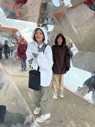 Two kids in hooded sweatshirts standing in a mirrored tunnel 