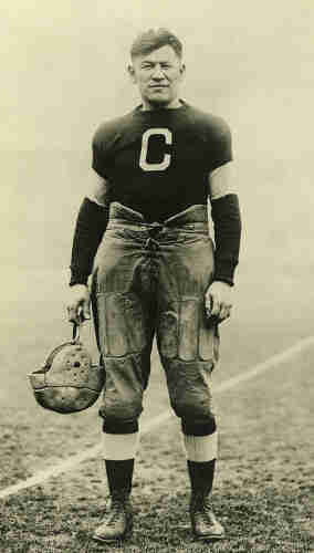 Jim Thorpe with the Canton Bulldogs, c. 1915 – c. 1920. He’s wearing a football uniform and holding his helmet in his right hand. By unattributed - Heritage Auctions, Public Domain, https://commons.wikimedia.org/w/index.php?curid=65611489