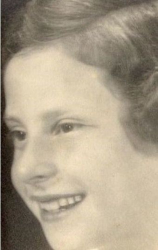 A close-up of the face of a smiling girl. She exposes her teeth. She has wavy hair.