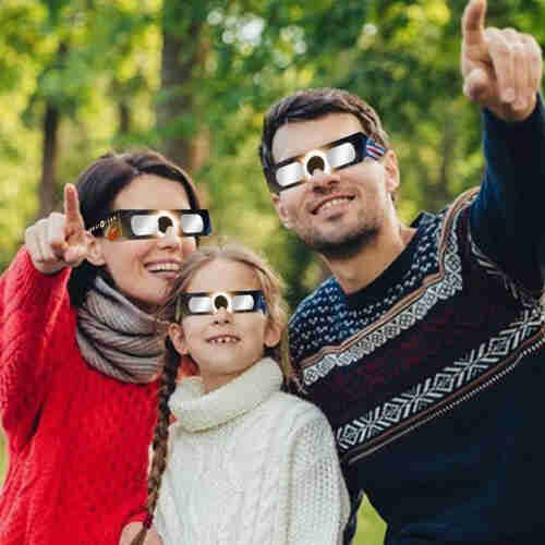 A mother and father with their daughter, all wearing sweaters and poorly photoshopped eclipse glasses. The parents are pointing at the sun while they all happily stare at the space inferno.