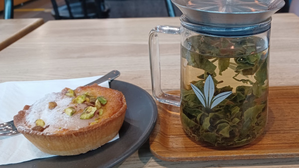 Tea leaves in glass vessel, a pear tart nearby